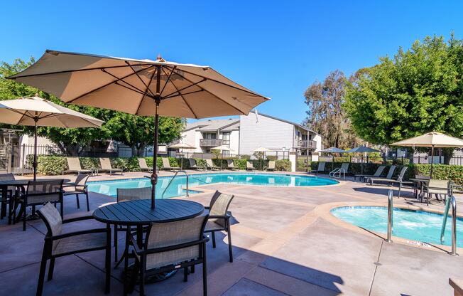 A pool area with a table and chairs and umbrellas.