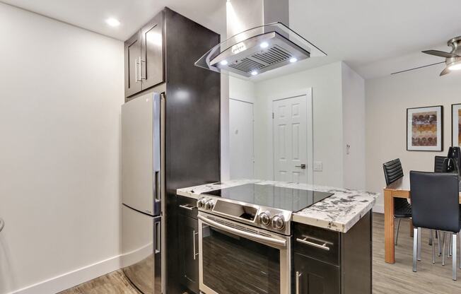 Kitchen with Stainless steel appliances, including electric range over range hood, granite countertops ,dark brown kitchen cabinets, wood style floors