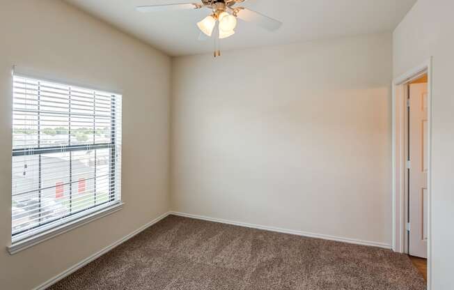 A room with a ceiling fan and a window with blinds.