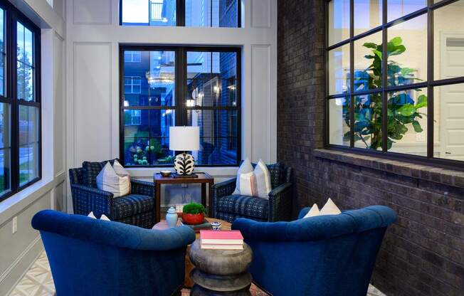 Two blue chairs are facing a table with a lamp and a vase on it.