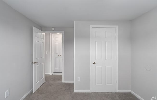 an empty bedroom with two doors and a carpeted floor