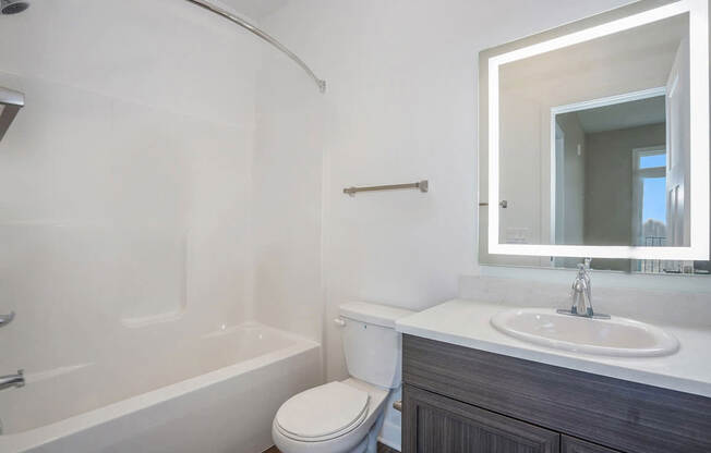 A bathroom with a bathtub, sink, and a lighted mirror at Meadowbrooke Apartment Homes in Kentwood, MI 49512