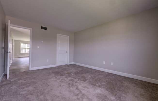 an empty living room with carpet and a door to a bedroom