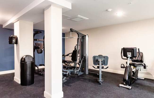 A gym with a rowing machine, a treadmill, a stationary bike, and a trash can.