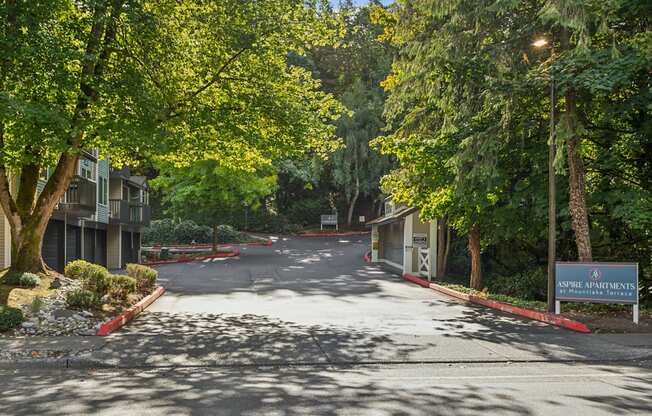 A tree-lined street with a sign for Aspire Apartments on the right.