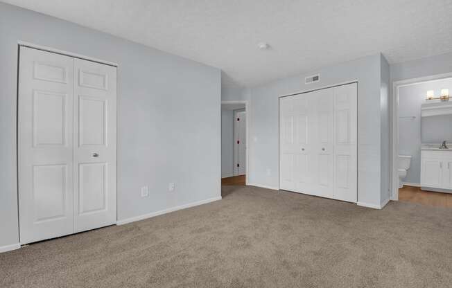 a bedroom with two doors and a bathroom in the background