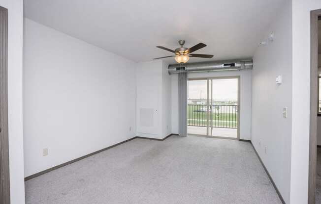 an empty living room with a ceiling fan and a door to a balcony