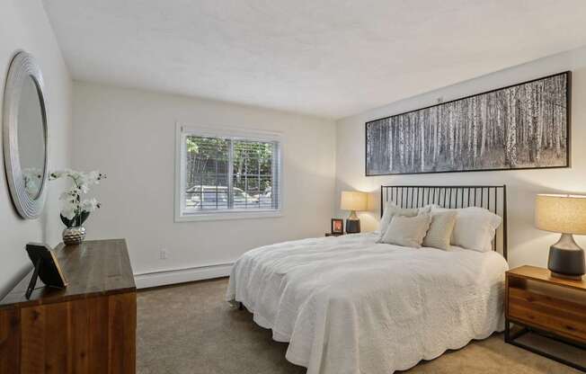 A bedroom with a large bed, a wooden dresser, and a painting on the wall.