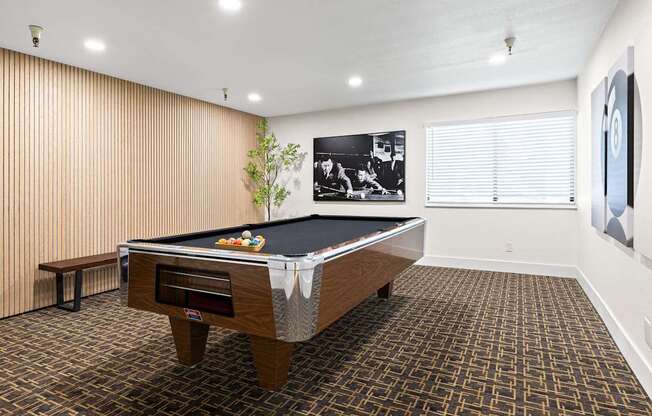 A pool table in a room with a bench and a picture on the wall.