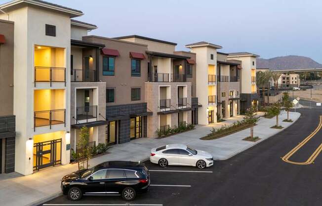 A row of modern townhouses with cars parked in front.