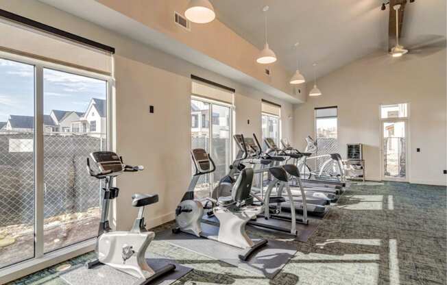 a gym with cardio machines and windows at the district flats apartments in lenexa