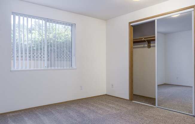 an empty bedroom with a large window and a mirrored closet