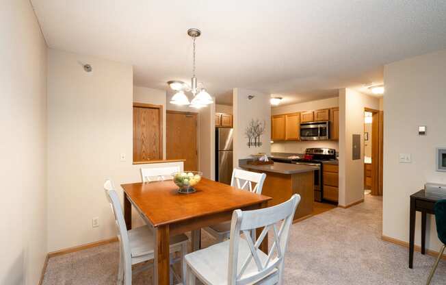 Kitchen and dining room with white chairs, wooden table, and a bright hanging lamp