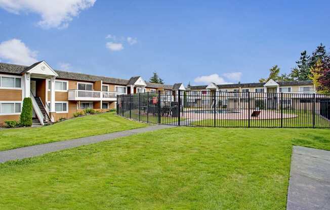 A well-maintained exterior here at Whispering Cedars with open green lawns, apartment buildings with private balconies, and a fenced outdoor pool area, creating a welcoming and community-focused environment.
