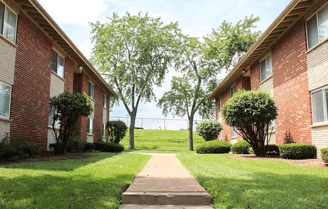 a walkway between two apartment buildings with grass and trees