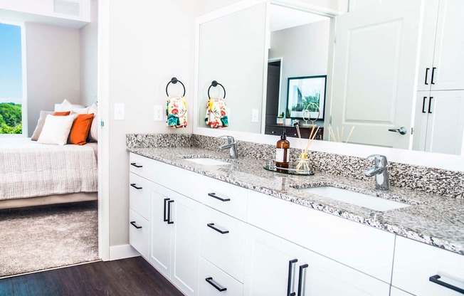 En suite bathroom vanity with granite countertops, stain-resistant plank flooring, and a double sink seamlessly connecting to the luxurious master bedroom.