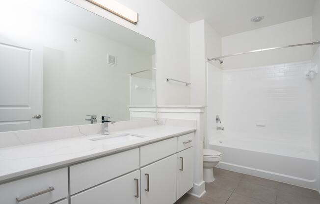 a bathroom with white cabinets and a white toilet next to a white bathtub with a shower