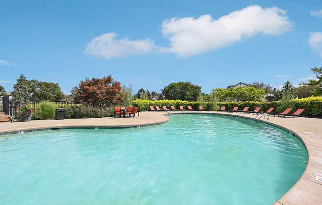 A large outdoor swimming pool surrounded by red chairs and greenery.