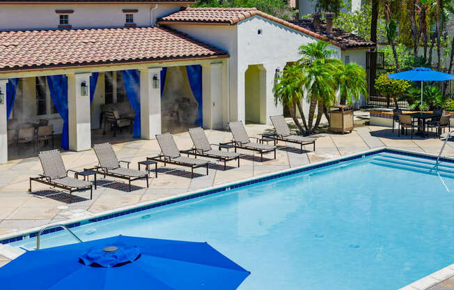 A pool with a blue umbrella and chairs around it.