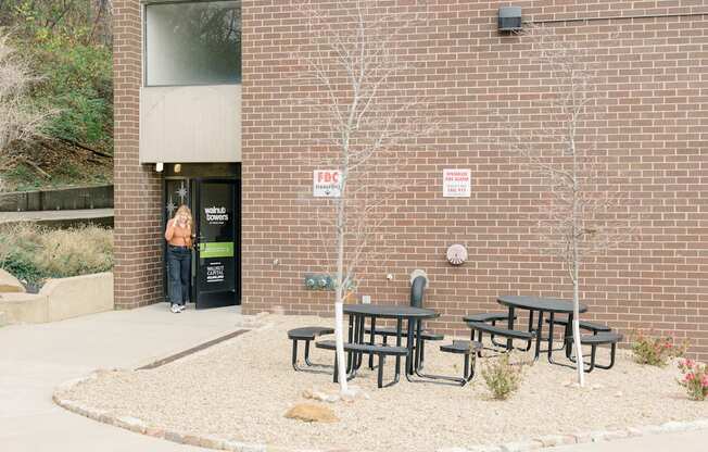A woman stands in the doorway of a brick building with a sign that says "No Parking" on the wall.