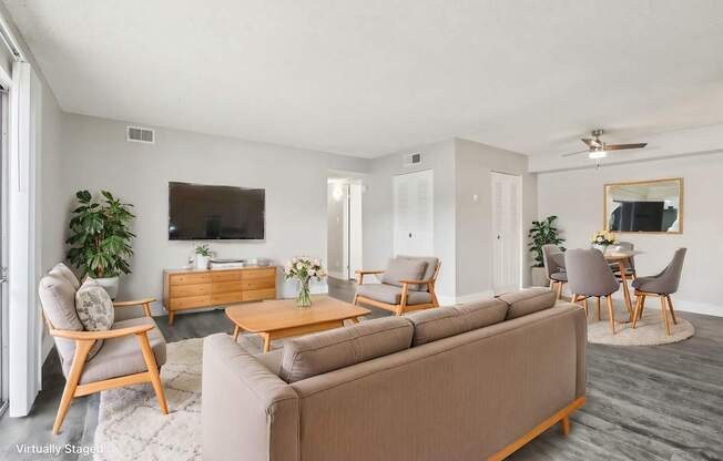 A living room with a brown sofa, wooden chairs, and a TV on the wall.