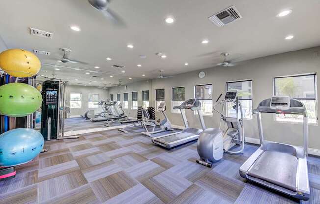 A gym with treadmills, elliptical machines, and exercise balls.