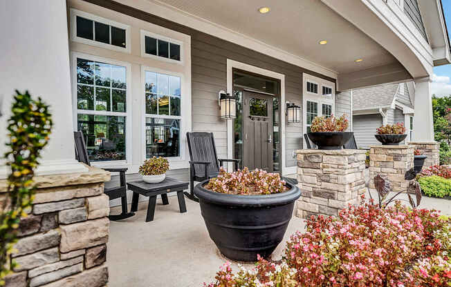 the front porch of a home with two chairs and a table and a large plant