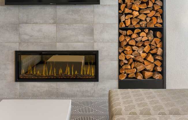 A modern fireplace with a black frame and a pile of wood to the right.
