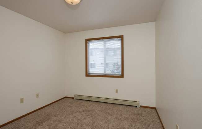 the living room of an empty home with carpet and a window. Fargo, ND Park Circle Apartments.