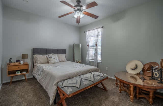 A bedroom with a bed, a table, and a ceiling fan.