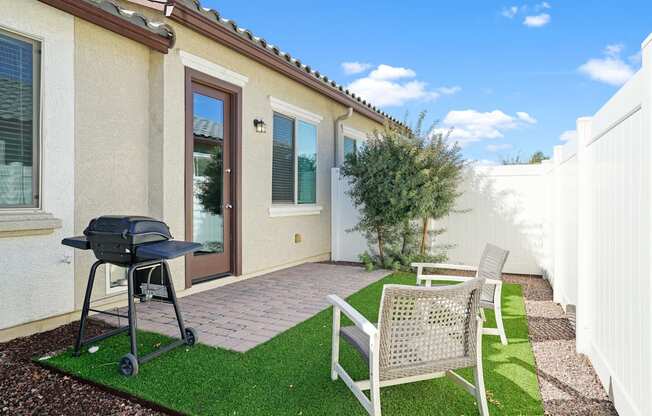 a backyard patio with a grill and two chairs