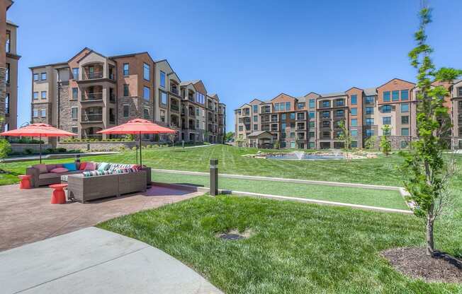 a grassy area with couches and umbrellas in front of an apartment complex