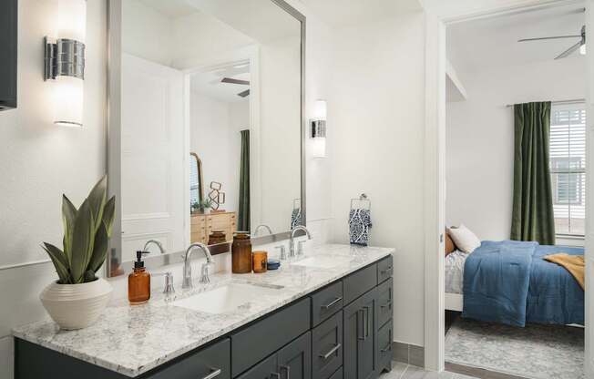 A bathroom with a large mirror, a sink, and a bed in the background.