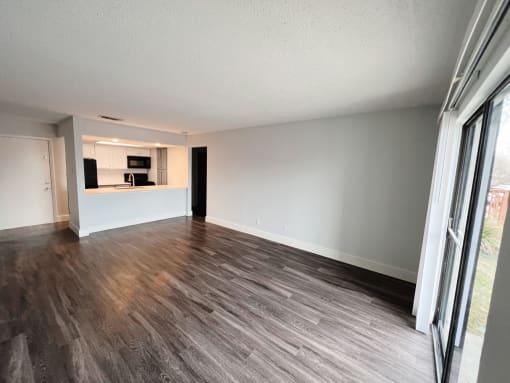 an empty living room with a large window and a kitchen