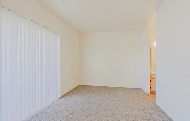 a spacious living room with white walls and a window with white blinds