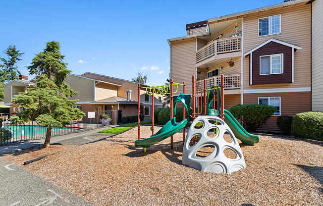 A playground with a slide and a climbing frame in front of a building.