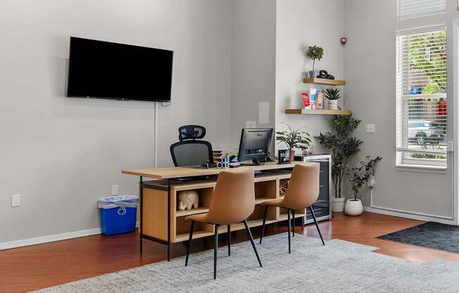 A room with a desk, chairs, and a TV mounted on the wall.