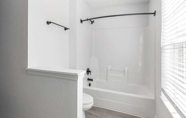 a white bathroom with a tub and a toilet and a window