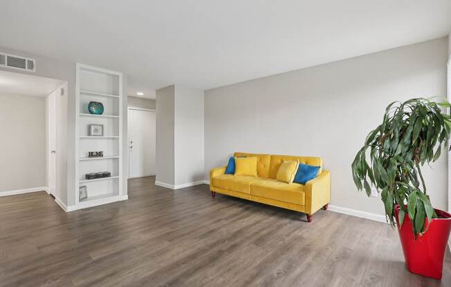 A living room with a yellow couch and a red planter.