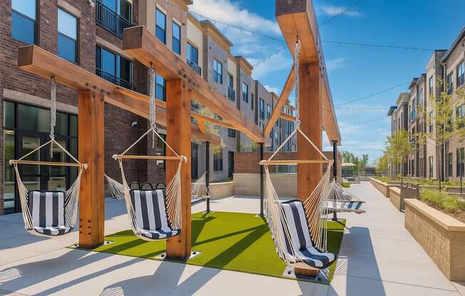 A wooden pergola with hanging chairs is in front of a building.
