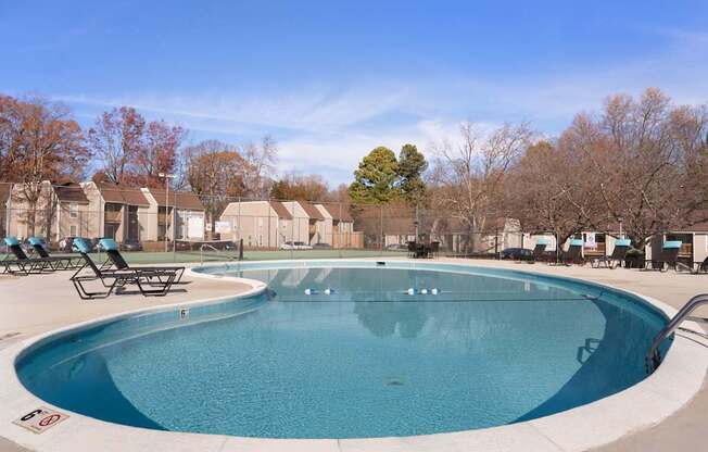 A large outdoor swimming pool surrounded by lounge chairs and trees.