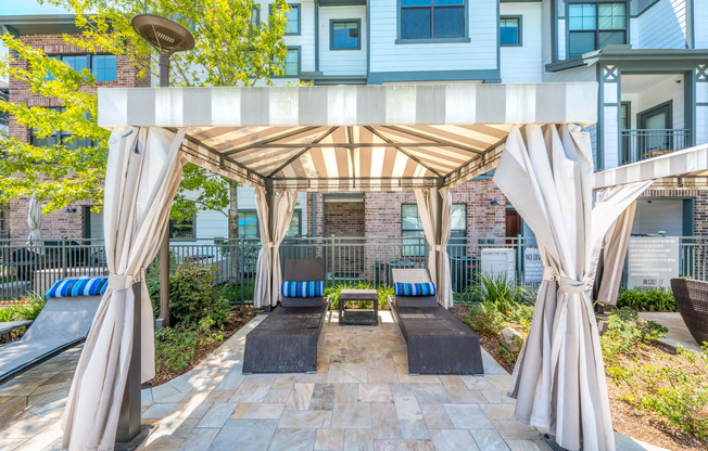 a pergola with lounge seating and a fire pit in front of an apartment building