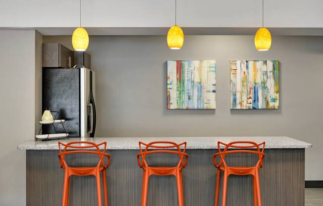 A kitchen with a refrigerator, two chairs and two paintings hanging on the wall.