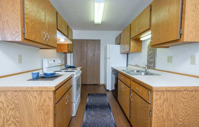 a kitchen with wood cabinets and white appliances and a blue rug. Fargo, ND Park Circle Apartments.