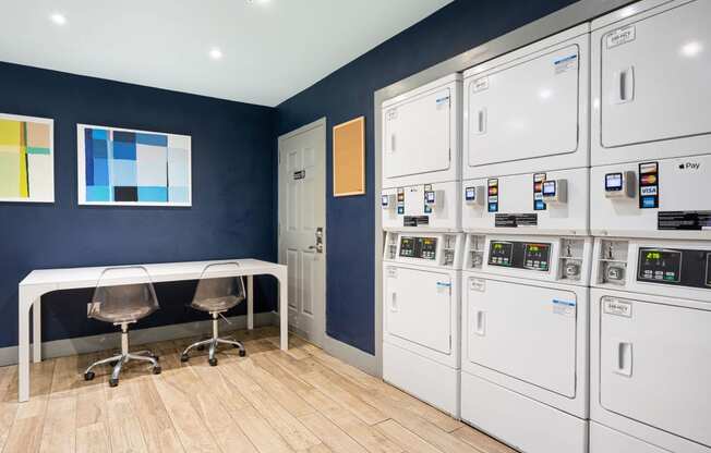 a laundry room with a table and chairs and a row of white washers and dryers