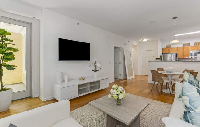 A living room with a white couch, a grey coffee table, and a flat screen TV mounted on the wall.