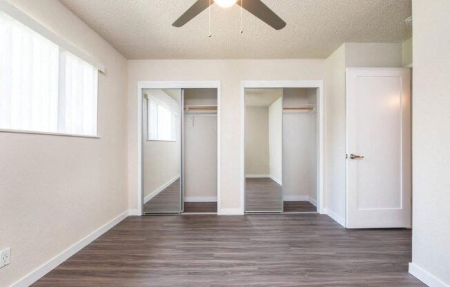 View from bedroom into sliding mirror door closet, has well lit window and ceiling fan