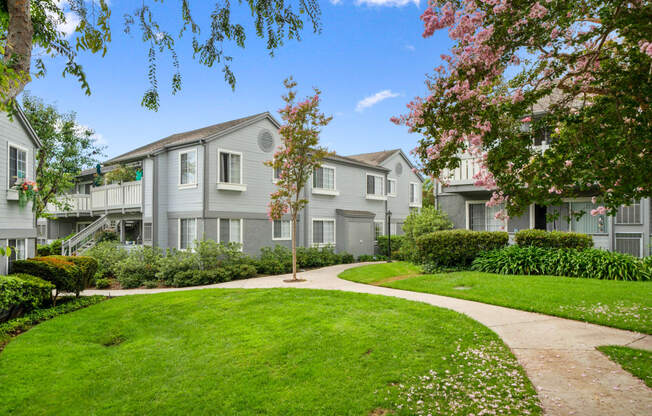 the view of an apartment building with a sidewalk and green grass