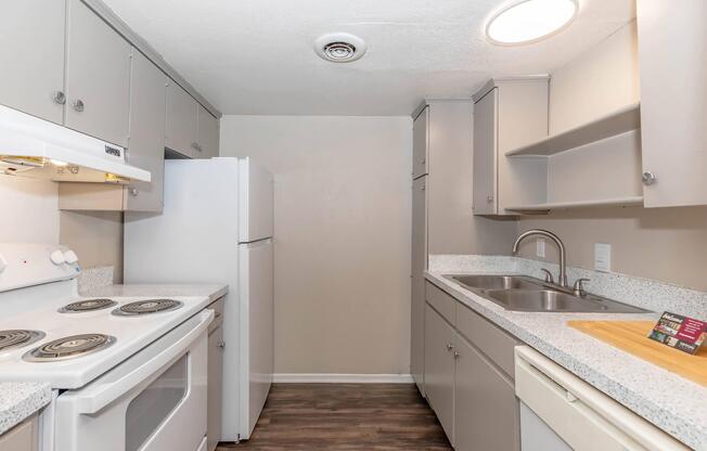 A compact kitchen featuring light gray cabinetry, a white stove, an oven, and a refrigerator. The countertop is gray with a matching sink and faucet. Natural light spills in from a ceiling fixture, enhancing the clean and modern design. The space is organized and functional, ideal for efficient cooking.