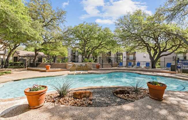A pool surrounded by trees and potted plants.